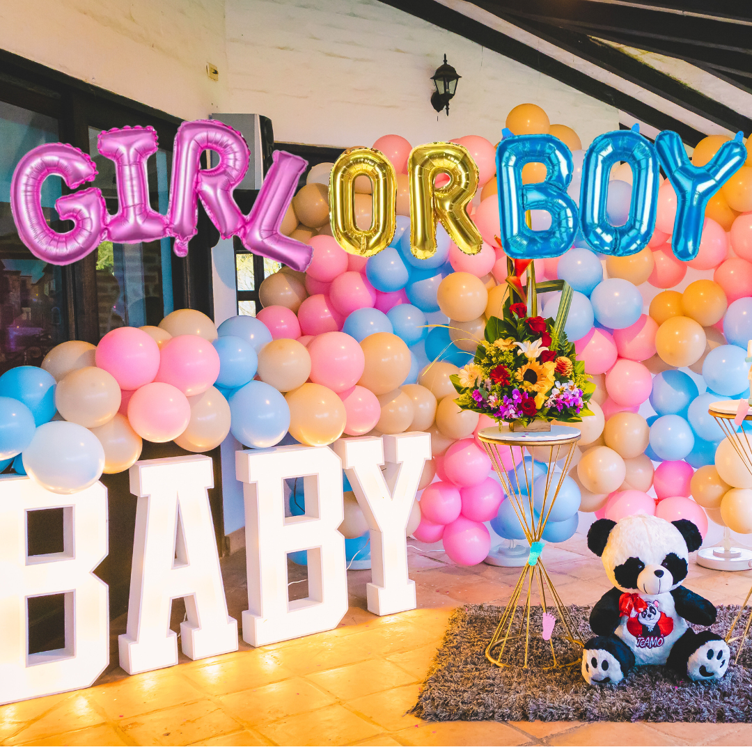 Gender reveal party setup with Girl or Boy foil balloons, pastel balloon arch, large BABY letters, and teddy bear decoration