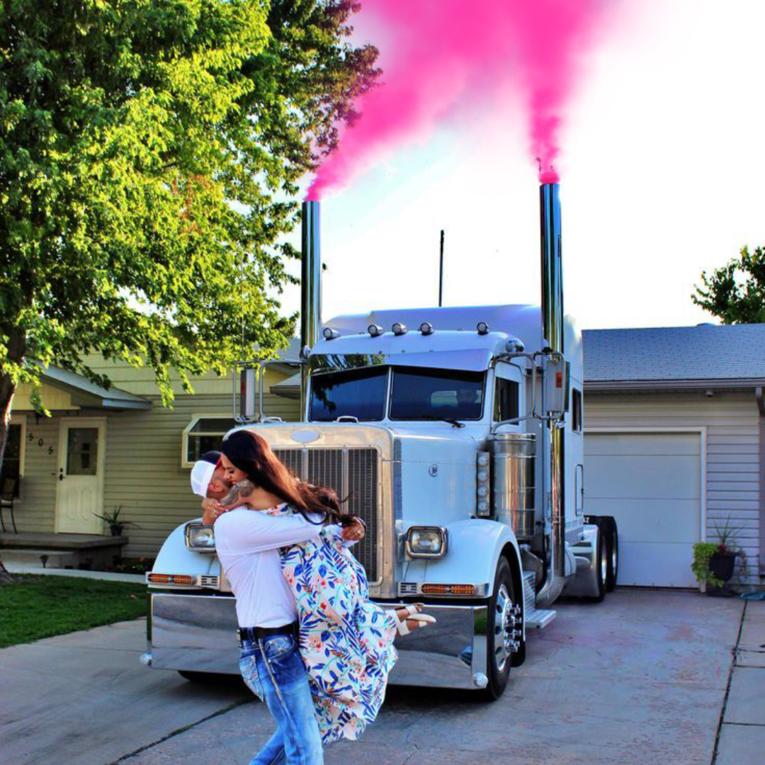 Couple celebrating in front of truck with pink smoke for gender reveal