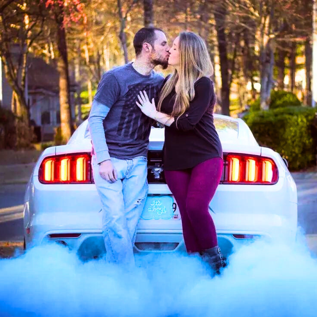 Couple in front of car with blue smoke for gender reveal