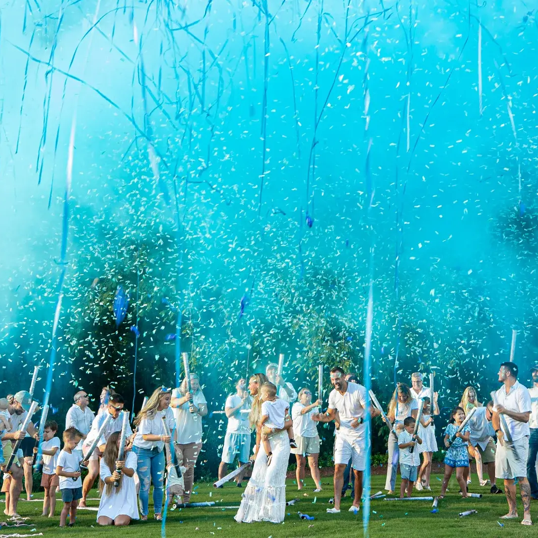 Family celebrating a baby boy announcement with blue confetti cannons outdoors.