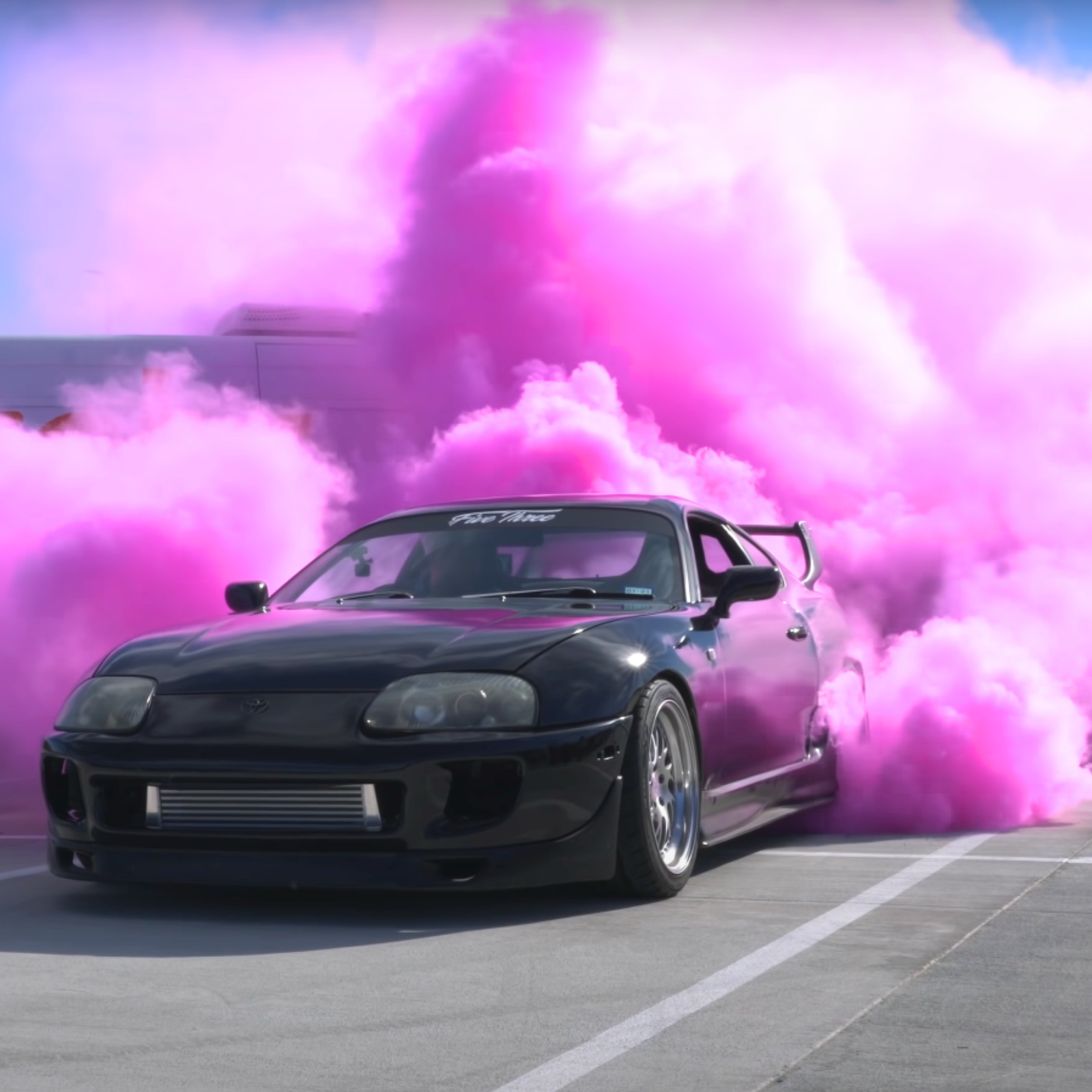 Gender reveal burnout with pink smoke behind a black sports car for a unique reveal event