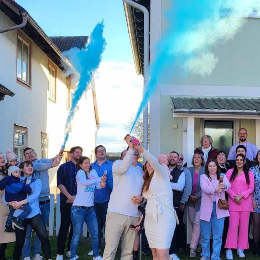 Group celebrating with blue gender reveal smoke cannons at a gender reveal party outdoors