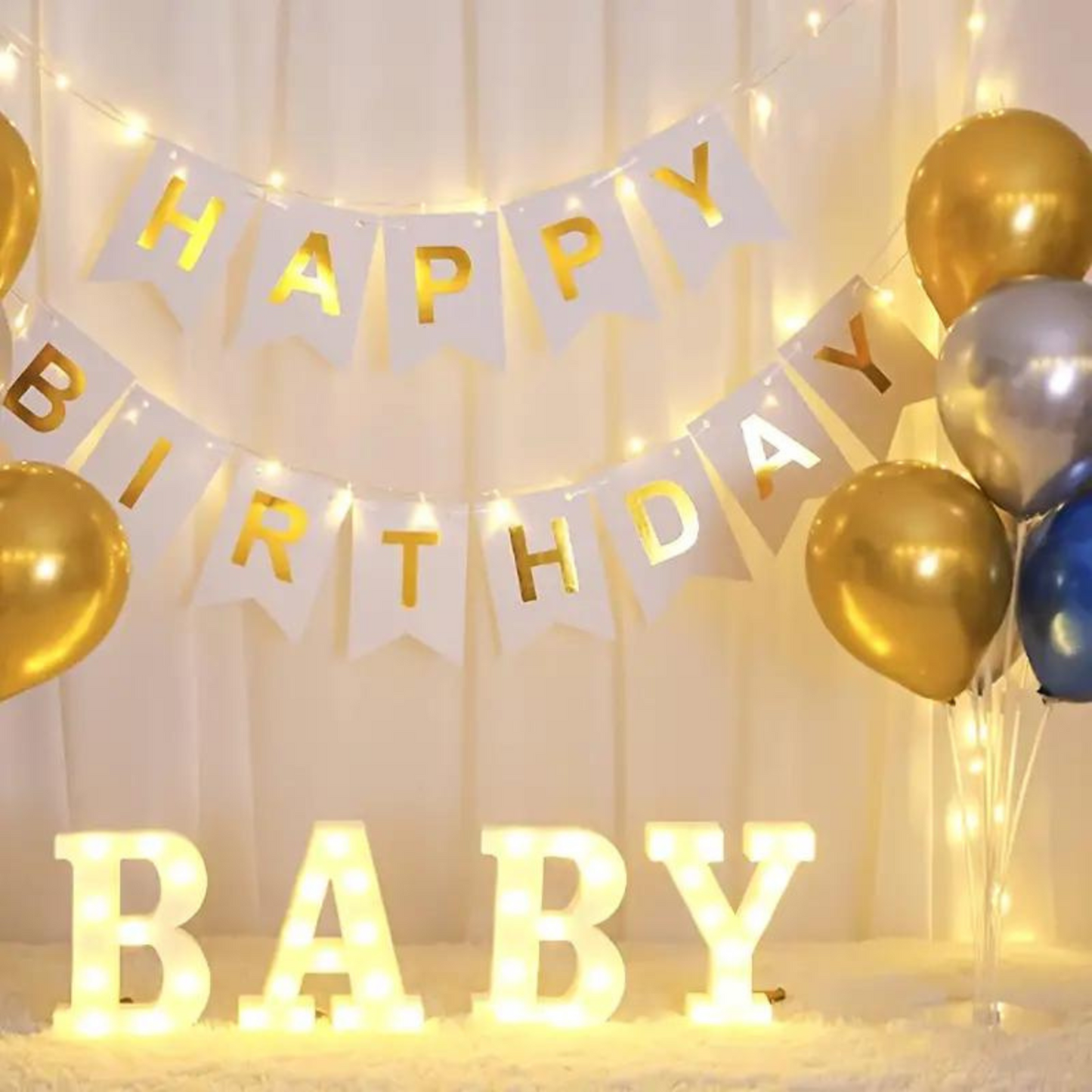 Happy Birthday banner with illuminated ‘BABY’ letters and gold and silver balloons in a festive setup.