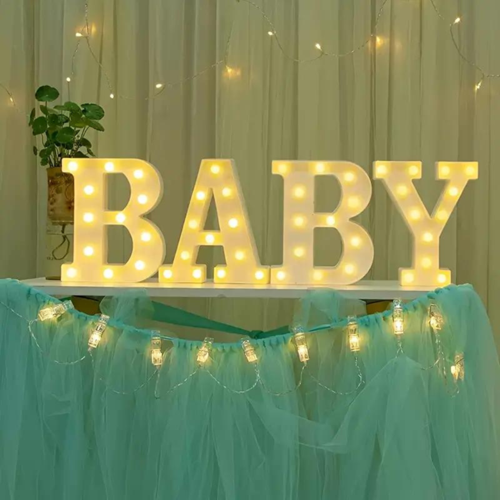 Illuminated ‘BABY’ letters on a table with blue tulle and string lights in a gender reveal party setup